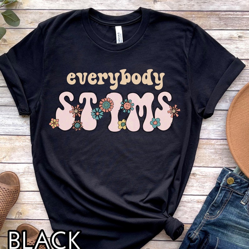 May include: Black t-shirt with the text "everybody stims" in pink and yellow letters with a retro font. The text is surrounded by colorful flowers.
