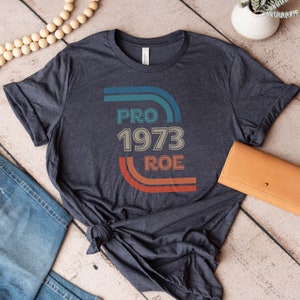 May include: A dark blue t-shirt with a vintage-style graphic that says "PRO 1973 ROE" in colorful text.