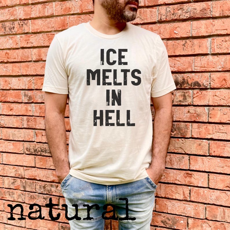 May include: Cream-colored t-shirt with the text "ICE MELTS IN HELL" in bold, black letters. The shirt is worn by a person in blue jeans, standing in front of a brick wall. The word "natural" is printed at the bottom of the image.