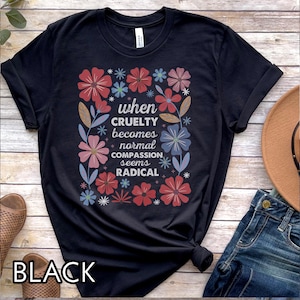 May include: Black t-shirt with a floral design and the text "when cruelty becomes normal compassion seems radical." The design includes red, pink, and blue flowers. The word "BLACK" is printed at the bottom of the shirt.