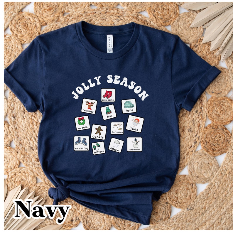 K&ouml;nnte beinhalten: Ein marineblaues T-Shirt mit einer wei&szlig;en Grafik der Worte "Jolly Season" in einer Retro-Schrift. Die Grafik enth&auml;lt auch verschiedene winterliche Symbole, wie zum Beispiel ein Rentier, einen Schneemann, einen Hut und einen Kranz.