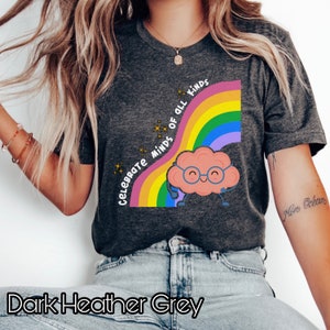 Pu&ograve; includere: Maglietta grigio scuro melange con un arcobaleno e un cervello di cartone animato con gli occhiali. Il testo "Celebrate Minds of All Kinds" &egrave; scritto sull'arcobaleno.
