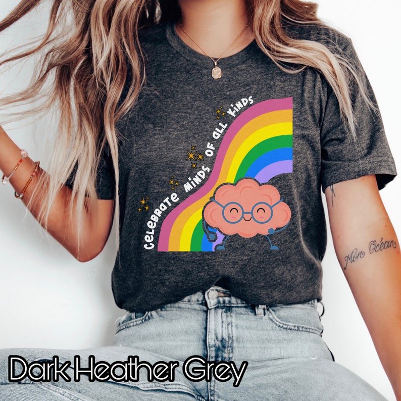 Pu&ograve; includere: Maglietta grigio scuro melange con un arcobaleno e un cervello di cartone animato con gli occhiali. Il testo "Celebrate Minds of All Kinds" &egrave; scritto sull'arcobaleno.