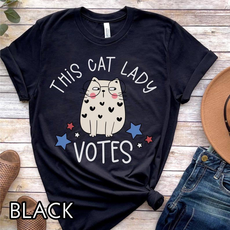 May include: Black t-shirt with a white graphic of a cat wearing glasses and the text "This Cat Lady Votes".
