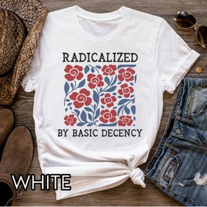 May include: White t-shirt with the text "RADICALIZED BY BASIC DECENCY" above a floral design of red flowers and blue leaves. The shirt is knotted at the waist.
