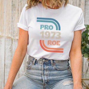 May include: White t-shirt with a retro-style graphic that says "PRO 1973 ROE" in blue, orange, and beige.