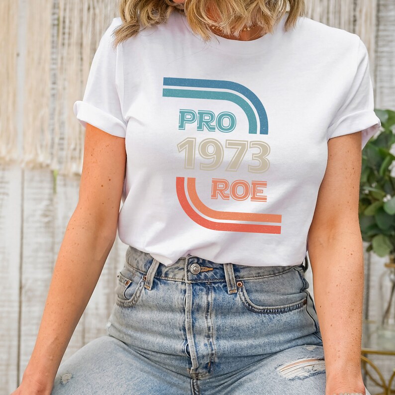May include: White t-shirt with a retro-style graphic that says "PRO 1973 ROE" in blue, orange, and beige.