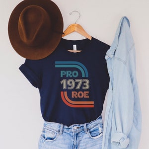May include: A navy blue t-shirt with a retro-style graphic that says "PRO 1973 ROE" in colorful text.