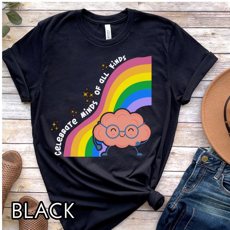Pu&ograve; includere: Maglietta nera con un arcobaleno e un cervello di cartone animato con gli occhiali. Il testo "Celebrate Minds of All Kinds" &egrave; sull'arcobaleno.