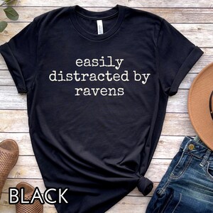 May include: Black t-shirt with the text "easily distracted by ravens" in white.