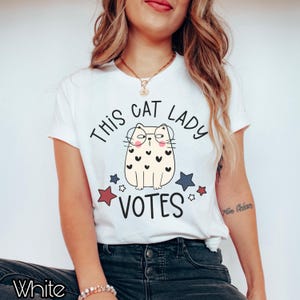 May include: White t-shirt with a cartoon cat wearing glasses and the text "This Cat Lady Votes" with red, white, and blue stars.