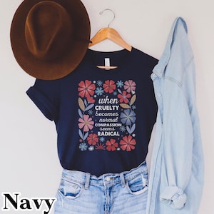 May include: Navy blue t-shirt with a floral design and the text "when cruelty becomes normal compassion seems radical." The shirt is displayed with a brown hat and a denim jacket.