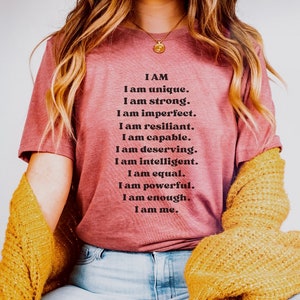May include: A pink t-shirt with the text "I AM I am unique. I am strong. I am imperfect. I am resilient. I am capable. I am deserving. I am intelligent. I am equal. I am powerful. I am enough. I am me."