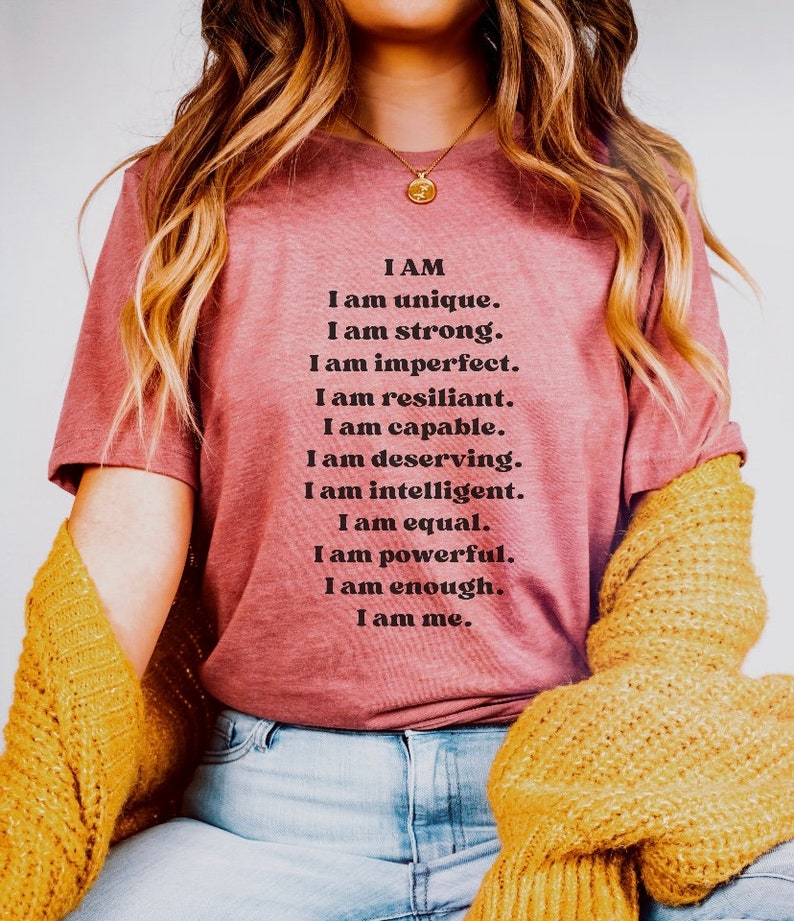 May include: A pink t-shirt with the text "I AM I am unique. I am strong. I am imperfect. I am resilient. I am capable. I am deserving. I am intelligent. I am equal. I am powerful. I am enough. I am me."