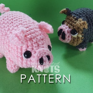 May include: Two crocheted pig plushies, one pink and one brown and gray, with black eyes and snouts. The pink pig is standing on a green surface. The text "complicated knots pattern" is visible below the pigs.