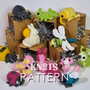 May include: A collection of crocheted amigurumi animal toys, including a bee, ladybug, snail, dragonfly, caterpillar, and a few others. The toys are displayed in small cardboard boxes with silver tinsel.
