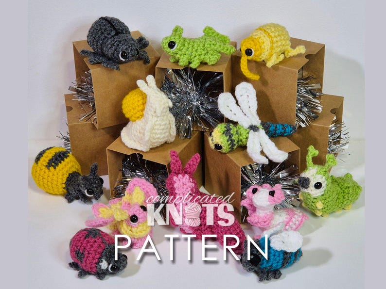 Puede incluir: Una colecci&oacute;n de juguetes de animales de ganchillo amigurumi, incluyendo una abeille, una mariquita, un caracol, una lib&eacute;lula, una oruga y algunos otros. Los juguetes se muestran en peque&ntilde;as cajas de cart&oacute;n con purpurina plateada.