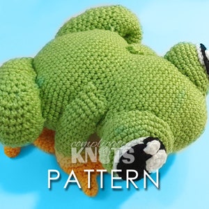 Könnte beinhalten: Ein grüner Häkel-Frosch mit orangenen Beinen und schwarzen und weißen Augen. Der Frosch liegt auf dem Rücken mit seinen Beinen in der Luft. Der Text "complete knots pattern" ist im Bild sichtbar.