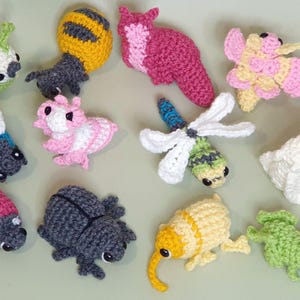 Puede incluir: Una colecci&oacute;n de 11 figuritas de animales de crochet, incluyendo una abeja, una mariquita, una mariposa, una lib&eacute;lula, una oruga, una rana, un escarabajo, un caracol, un conejito y dos otros insectos. Las figuritas est&aacute;n todas hechas con diferentes colores de hilo y tienen detalles elaborados.