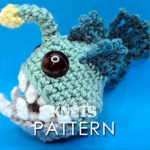 Peut inclure: Un jouet amigurumi en crochet en forme de poisson-pêcheur avec un gros œil, des dents blanches et une nageoire bleue. Le jouet est fait de fil bleu clair et bleu foncé. Le texte "complicated KNOTS PATTERN" est visible sur le jouet.