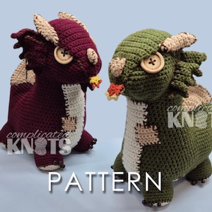 May include: Two crocheted dragon plushies, one deep burgundy and one olive green, each featuring cream-coloured belly patches, beige horns, wooden button eyes, and a small orange and yellow flame detail at the mouth. The text "complicated KNOTS PATTERN" is visible.