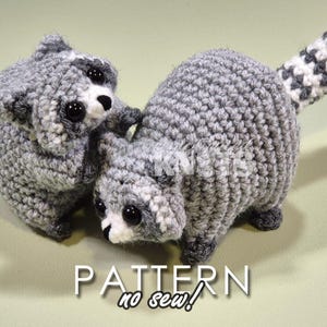 May include: Two crocheted raccoon plushies, one with a tail, both with black eyes and white accents. The plushies are gray and white and have a no-sew pattern.