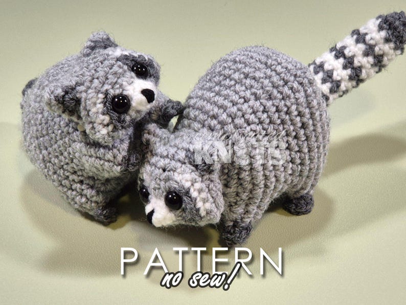 May include: Two crocheted raccoon plushies, one with a tail, both with black eyes and white accents. The plushies are gray and white and have a no-sew pattern.