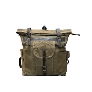 May include: Olive green canvas backpack with black leather accents. Features include a flap closure with buckles, a front pocket, and side pockets. The bag has a roll-top design and adjustable straps.