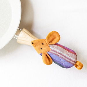 May include: A purple and orange striped pot holder shaped like a mouse with a wooden handle attached to the back.