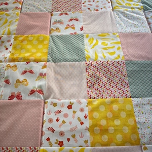 Könnte beinhalten: Ein Patchwork-Quilt mit verschiedenen Stoffen in Rosa, Gelb, Weiß und Grün. Der Quilt besteht aus quadratischen Blöcken mit Blumen-, Schmetterlings- und Tupfenmustern. Ein handgefertigtes Produkt.
