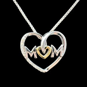 May include: A silver necklace with a heart-shaped pendant. The pendant features the word "MOM" in silver letters, with a gold heart in the center. Small clear stones are set around the edge of the heart.