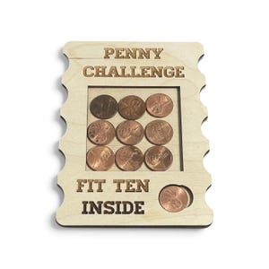 May include: A light-colored wooden board with the laser-engraved text PENNY CHALLENGE and FIT TEN INSIDE. The board features a square cutout containing nine copper-colored pennies arranged in a grid, with one additional penny in a circular slot.