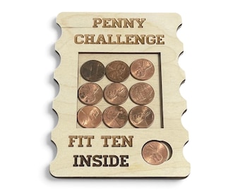 May include: A light-colored wooden board with the laser-engraved text PENNY CHALLENGE and FIT TEN INSIDE. The board features a square cutout containing nine copper-colored pennies arranged in a grid, with one additional penny in a circular slot.