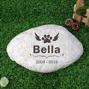 May include: A white stone memorial with a paw print, wings, and halo engraved on it. The text "Bella 2005-2019" is also engraved on the stone.