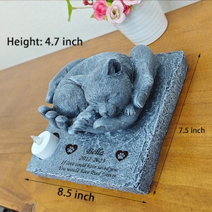 May include: A gray stone memorial with a sleeping cat sculpture. The memorial has a small candle holder and a personalized inscription that reads "Bella 2012-2023 If love could have saved you, you would have lived forever."
