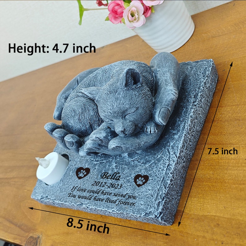 May include: A gray stone memorial with a sleeping cat sculpture. The memorial has a small candle holder and a personalized inscription that reads "Bella 2012-2023 If love could have saved you, you would have lived forever."
