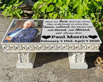 Puede incluir: Un banco conmemorativo blanco con una parte superior rectangular y patas ornamentadas. El banco presenta una foto de un hombre y una inscripción: "Aquellos a quienes amamos no se van... Todavía amados, todavía extrañados... Paul Morris 3 de febrero de 1962 - 9 de abril de 2020."