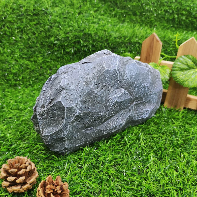 May include: A gray, textured rock with a rough surface. The rock is sitting on a bed of green artificial grass.