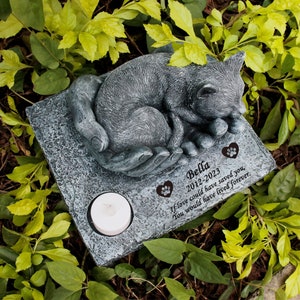 May include: A gray concrete memorial with a sleeping cat sculpture. The memorial has a small candle holder and a personalized inscription that reads "Bella 2012-2023 If love could have saved you, You would have lived forever."