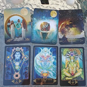 Könnte beinhalten: Eine Sammlung von Tarotkarten mit mystischen Illustrationen, darunter Karten mit der Aufschrift "Self-reflection", "Focus" und "Attraction". Die Karten zeigen Bilder von Figuren, Himmelskörpern und symbolischen Elementen. Verschiedene Kristalle sind um die Karten angeordnet.