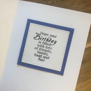May include: A white card with a blue border and a message that reads "Hope your Birthday is filled with lots of friends, family, food and fun!"