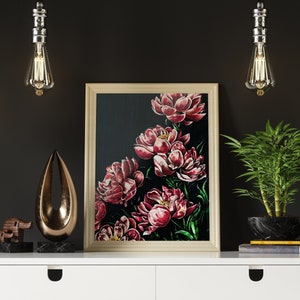 May include: A white desk with two drawers and wooden legs, featuring a framed painting of red peonies on a black background, a gold metal sculpture, a wooden elephant figurine, a potted green plant, and three hanging light bulbs.