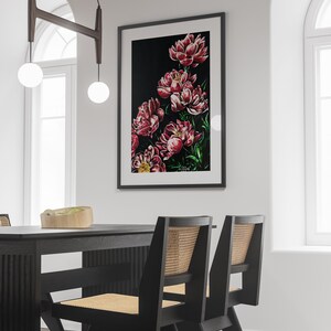 K&ouml;nnte beinhalten: Ein gerahmtes Gem&auml;lde von rosa Pfingstrosen auf schwarzem Hintergrund. Das Gem&auml;lde h&auml;ngt an einer wei&szlig;en Wand in einem modernen Esszimmer mit einem schwarzen Tisch und zwei St&uuml;hlen.