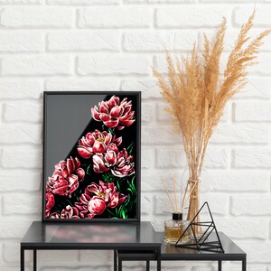 May include: A black framed print of a floral painting featuring a bouquet of red peonies on a black background. The print is displayed on a black table with a vase of dried pampas grass and a decorative metal stand.