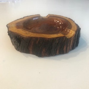 May include: A wooden ashtray with a natural bark finish. The ashtray is shaped like a tree stump and has a deep well for ashes.