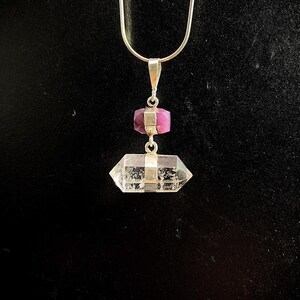 May include: A silver chain necklace with a clear crystal pendant and a small pink gemstone accent.