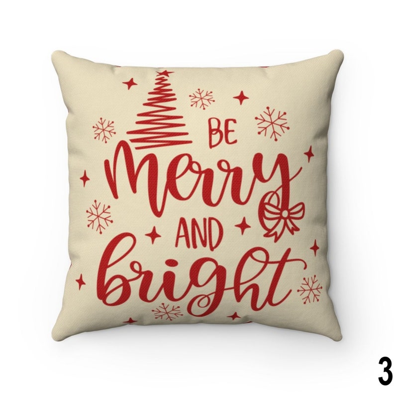 Pu&ograve; includere: Cuscino quadrato con sfondo color crema. Il cuscino presenta le parole "Be Merry and Bright" in corsivo rosso, insieme a un albero di Natale, fiocchi di neve e stelle. Un oggetto decorativo festivo per la casa.