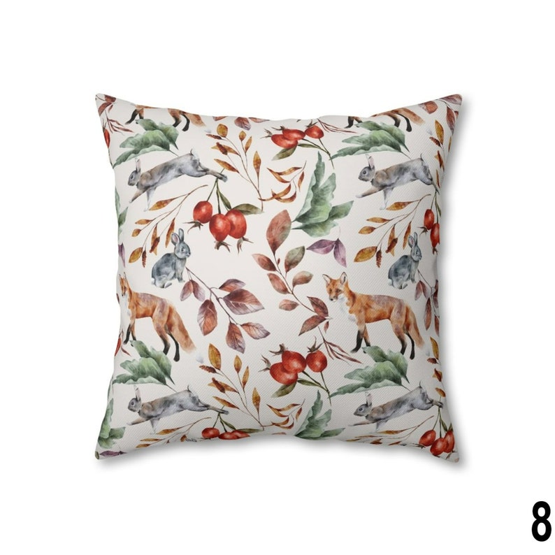 May include: Square throw pillow with a repeating pattern of foxes, rabbits, and berries among autumn leaves. The design features watercolor illustrations in shades of orange, gray, green, and brown on a cream background.
