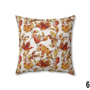 May include: Square throw pillow with a repeating pattern of autumn leaves and berries in shades of orange, red, and yellow on a white background. The pillow has a soft, inviting appearance, perfect for seasonal decor.