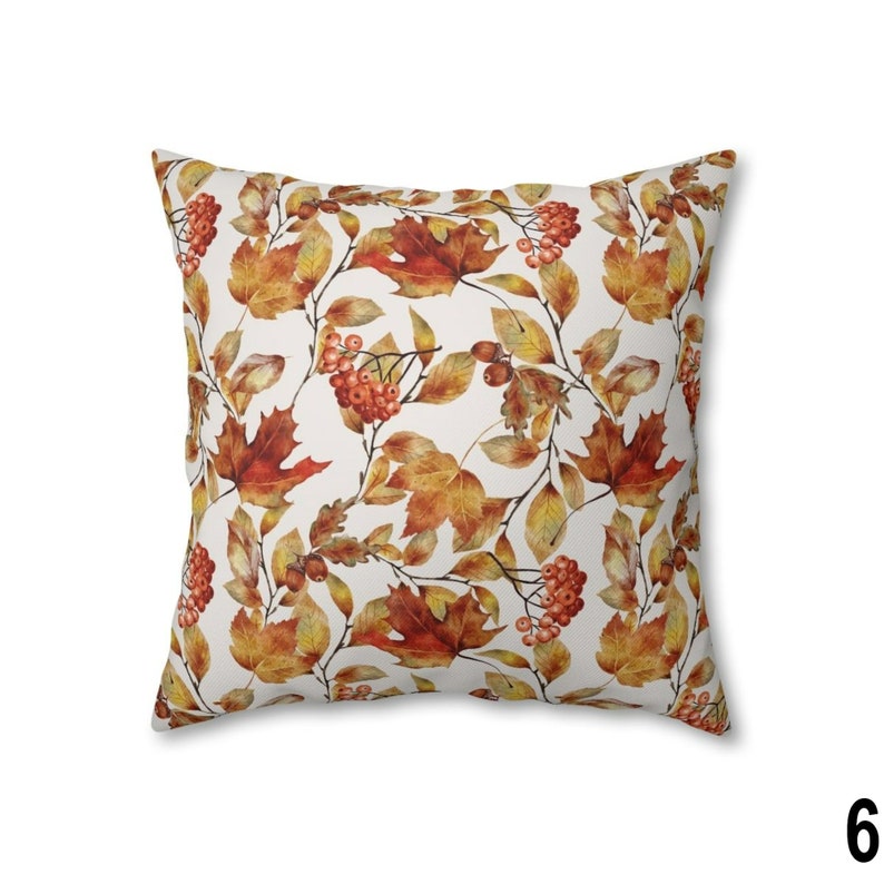 May include: Square throw pillow with a repeating pattern of autumn leaves and berries in shades of orange, red, and yellow on a white background. The pillow has a soft, inviting appearance, perfect for seasonal decor.